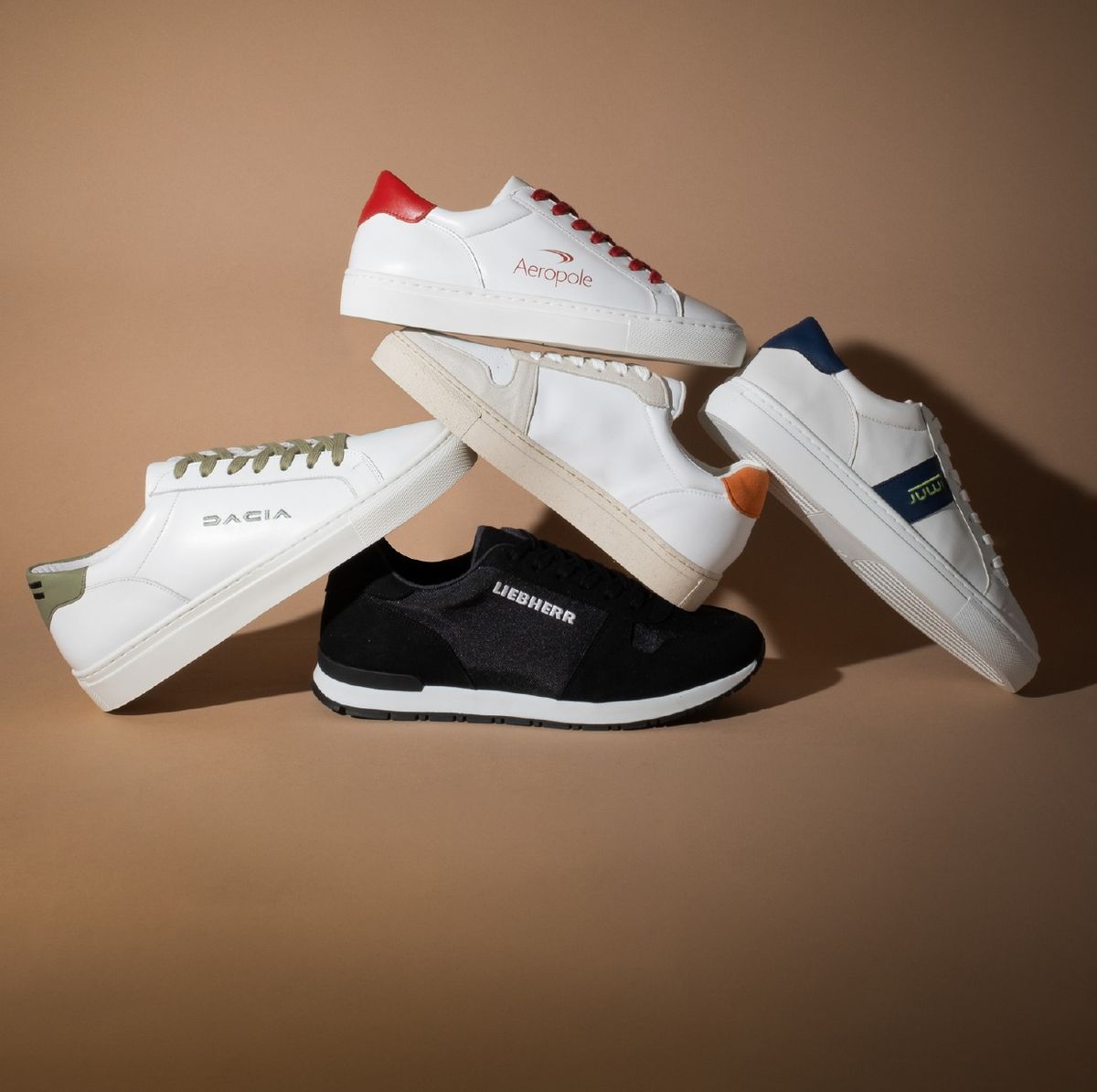 Mehrere individuell gestaltete Firmen-Sneaker gestapelt — weiße Leder-Sneaker mit farbigen Fersen und Schnürsenkeln sowie ein schwarzer Runner